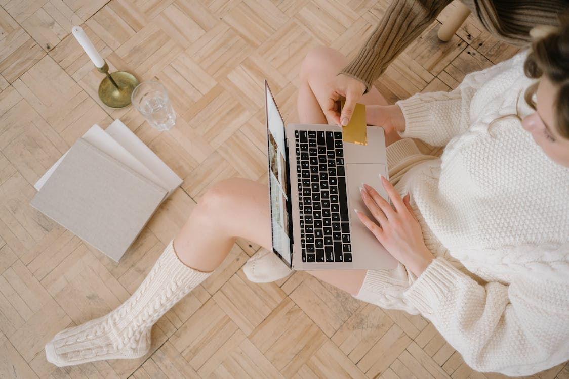 A person in cozy clothing shopping online with a laptop and holding a credit card