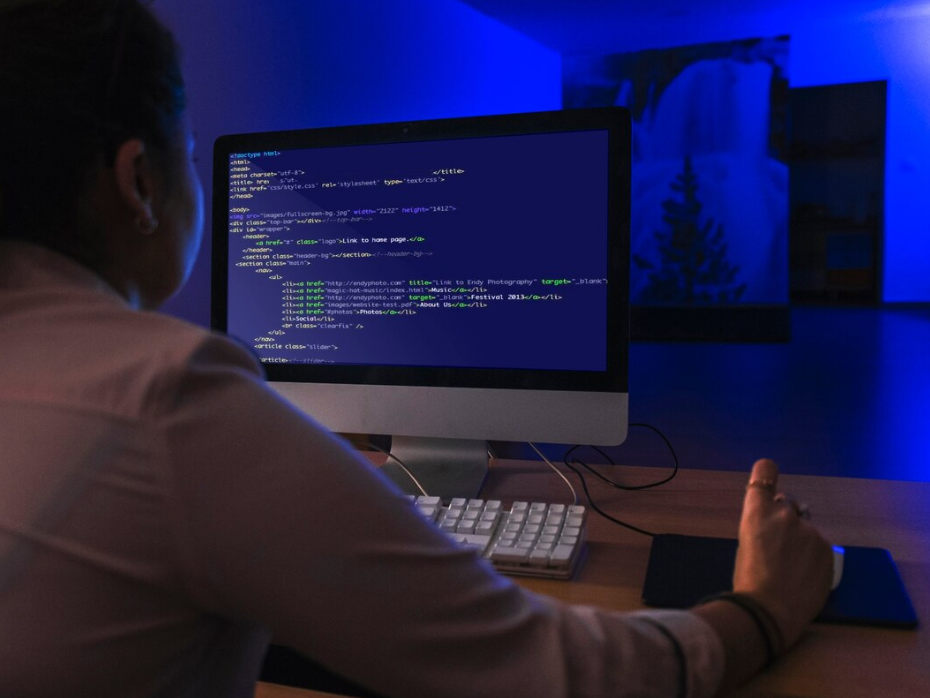 A developer coding on a desktop computer in a dimly lit workspace