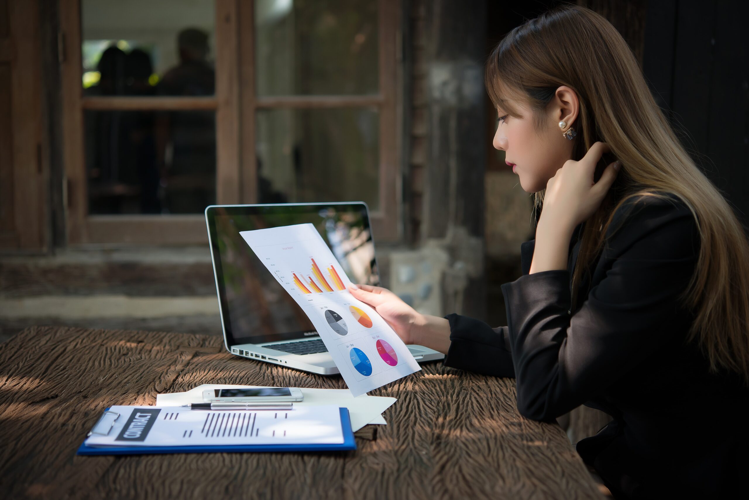 A woman reviewing data charts while working on her laptop outdoors.