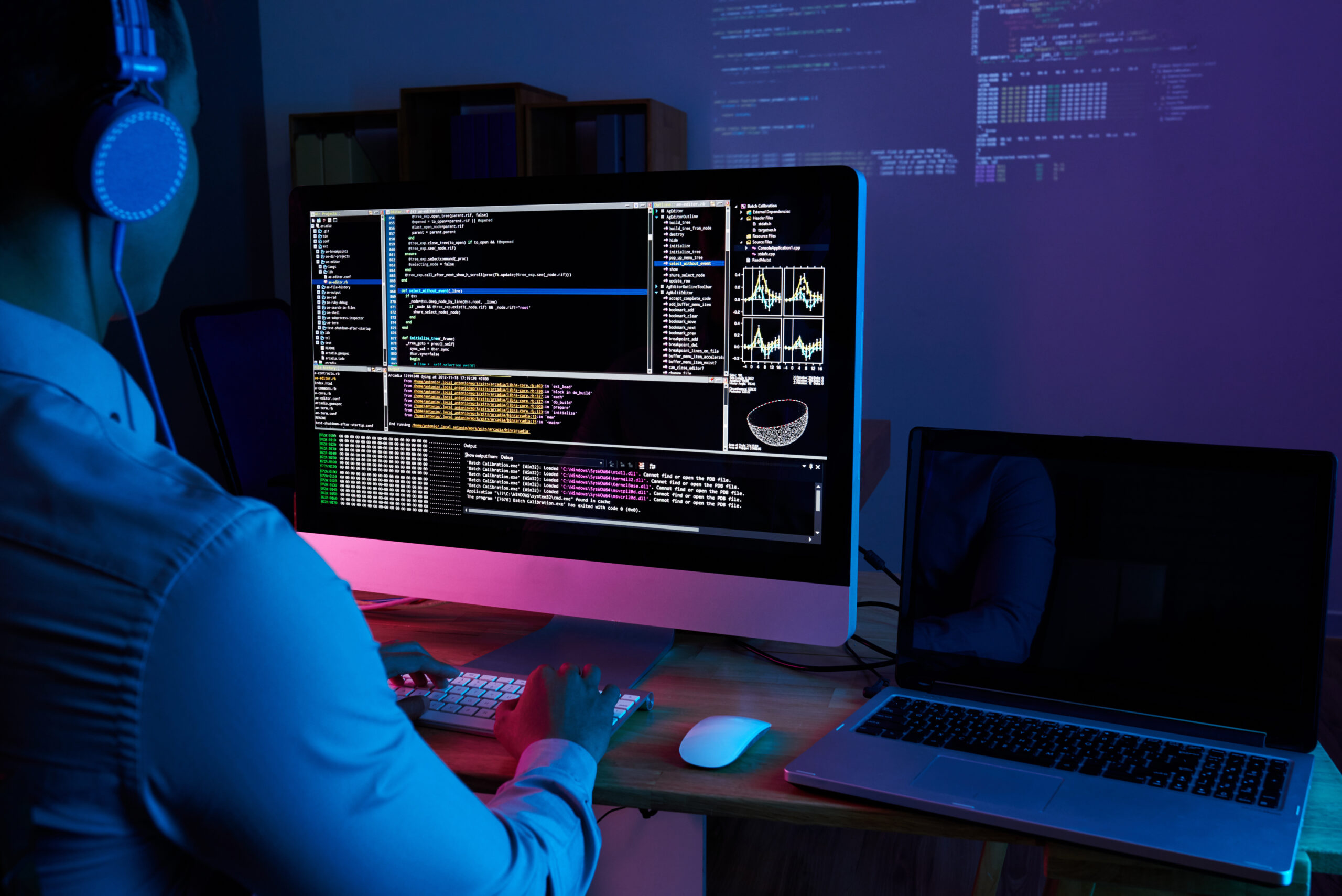 A developer working at a desktop computer with code and data visualizations
