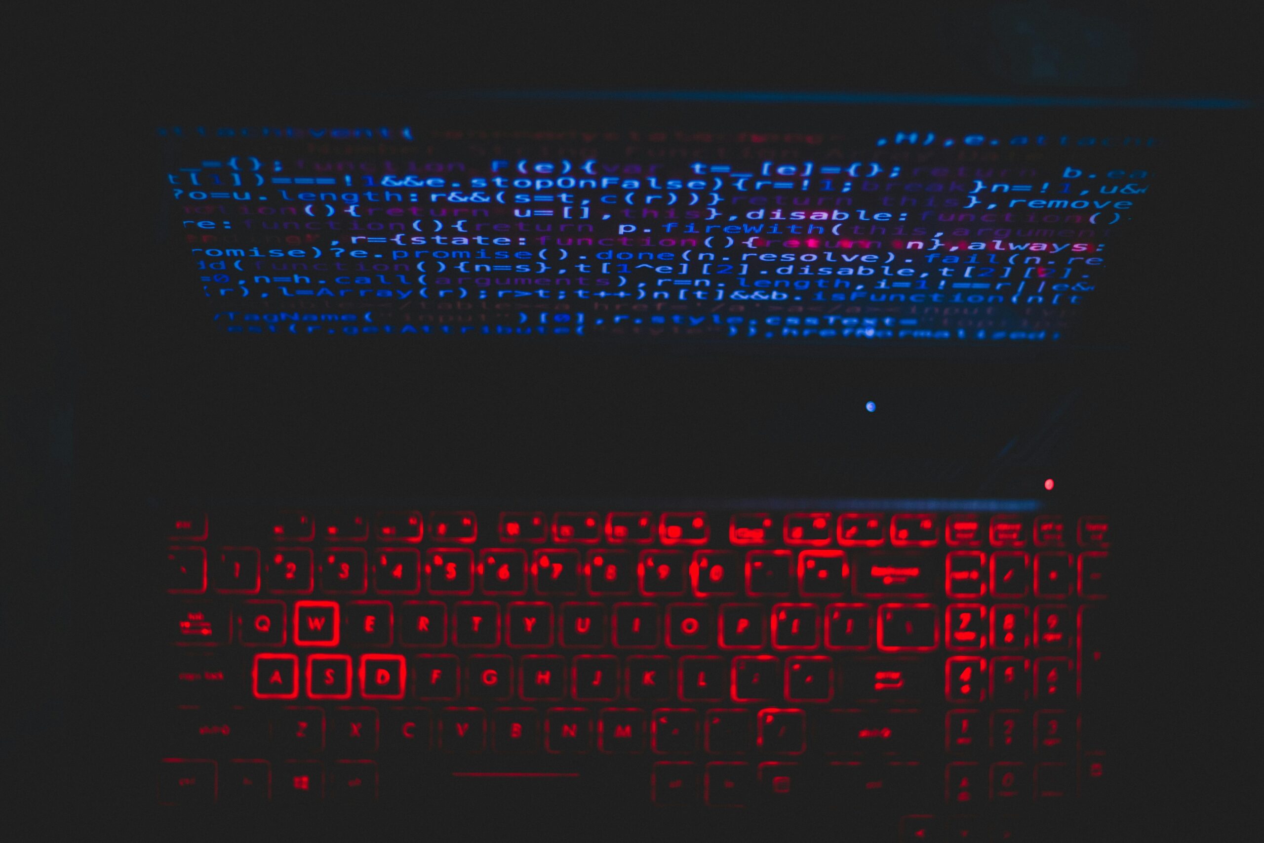 A close-up of a laptop with red backlit keys and lines of code displayed on the screen